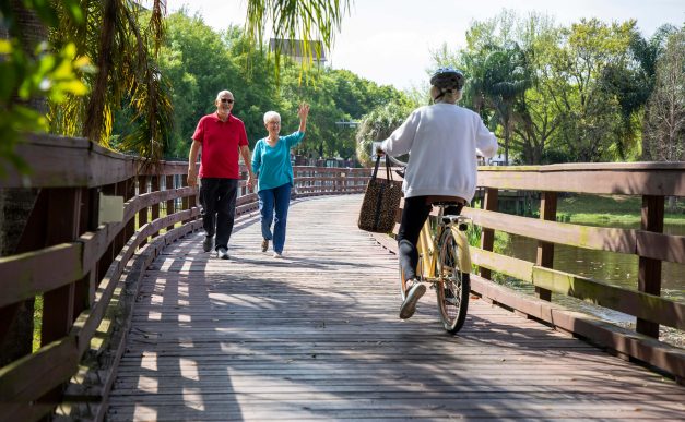 Senior couple walking across a bridge waiving at a older woman riding a bike