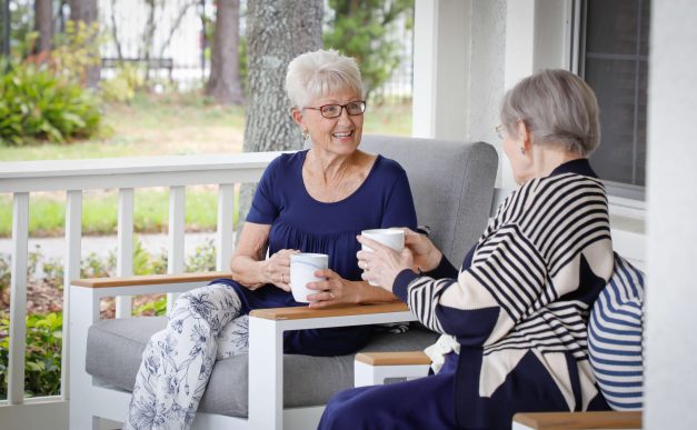 Two older adult women engaged in conversation on covered front porch