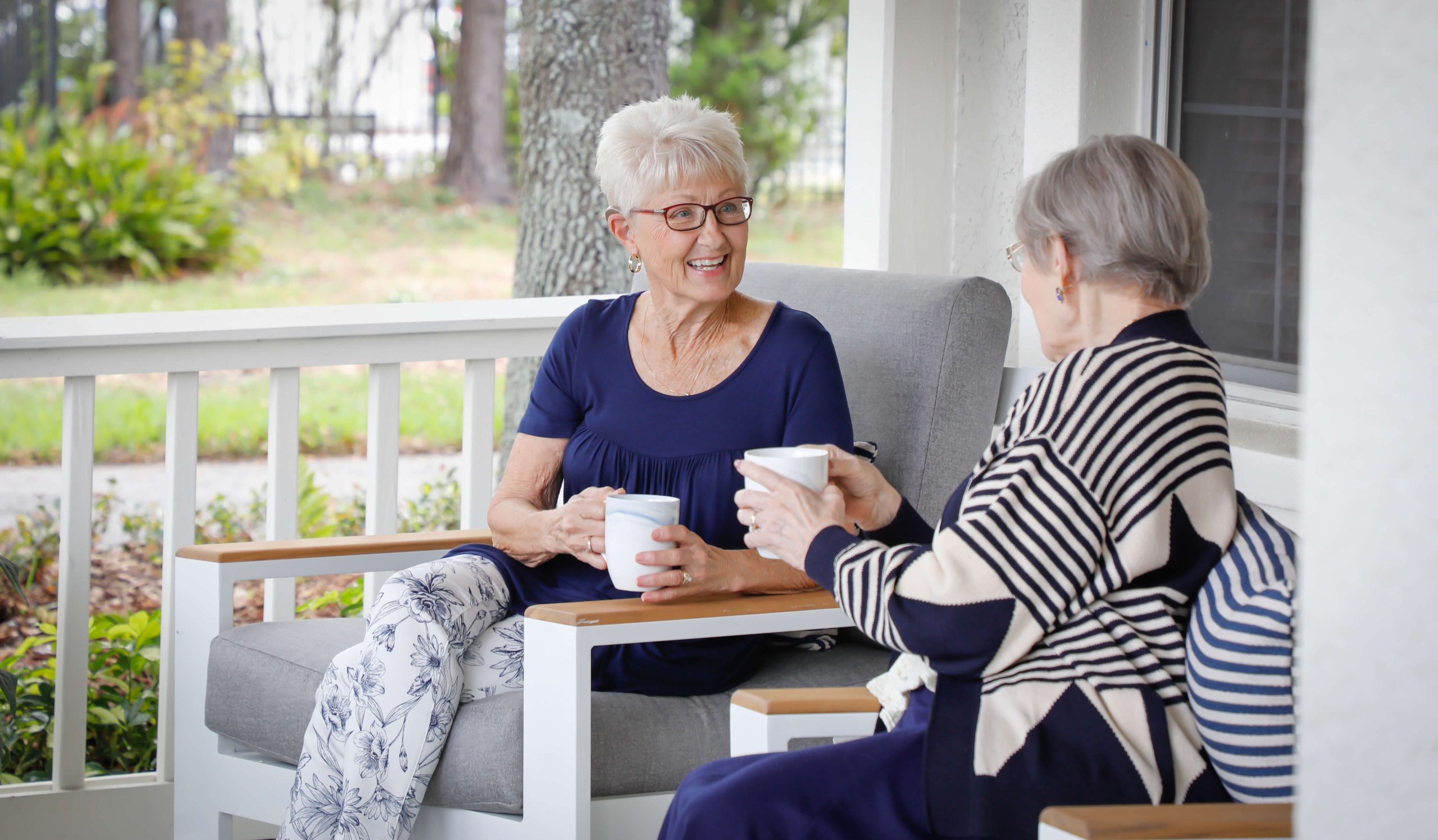 Two older adult women engaged in conversation on covered front porch